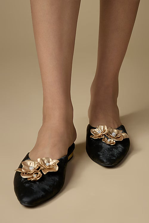 Black shoes with gold floral embellishments worn by a person on a beige background